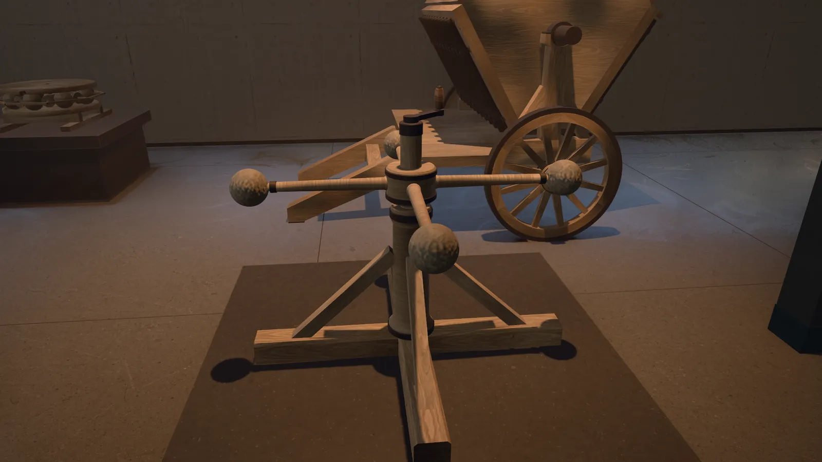 The flywheel up close: a wooden spindle on a cross of beams with struts, four arms at the top with stone balls at their ends, and a small crank. Behind it the gun with three rows of barrels, its spoked wheel in front. On the left the ball bearing on a dark plinth. A still from the museum's film.
